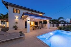 A modern house with a swimming pool, outdoor seating, and a well-lit patio area.