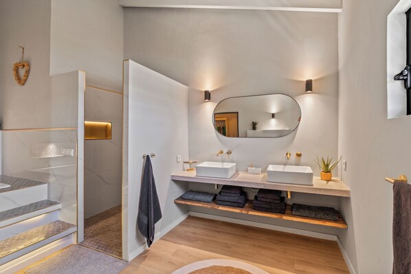 A modern bathroom with a large mirror, two sinks, and a shower area.