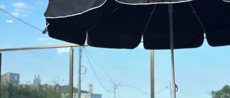 Une terrasse avec un parasol noir, un canapé avec des coussins et une vue sur la mer et les éoliennes.