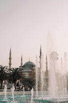 Una fuente con múltiples chorros de agua frente a una mezquita con cúpula y minaretes.