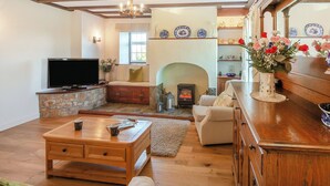 A living room with a stone fireplace, wooden furniture, a television, and a vase with flowers.