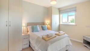 A bedroom with a bed, bedside lamps, a wardrobe, a window, and a ceiling light fixture.
