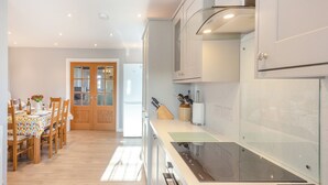 A modern kitchen with white cabinets, a built-in stove, and a dining area with wooden chairs and a table.