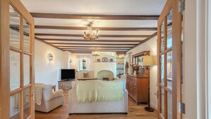 A room with a fireplace, a television, a sofa, a dining table, and wooden beams on the ceiling.