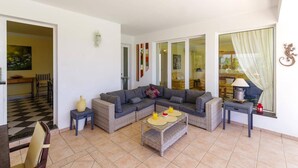 A living room with a grey sectional sofa, a wicker coffee table, and a dining area with a checkered floor.