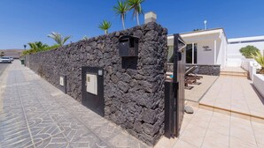 A stone-walled building with a small window and a door, a paved walkway, and a pool area with lounge chairs.