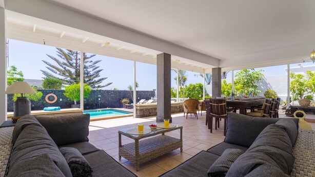 A covered outdoor seating area with a pool, lounge chairs, and a dining table.