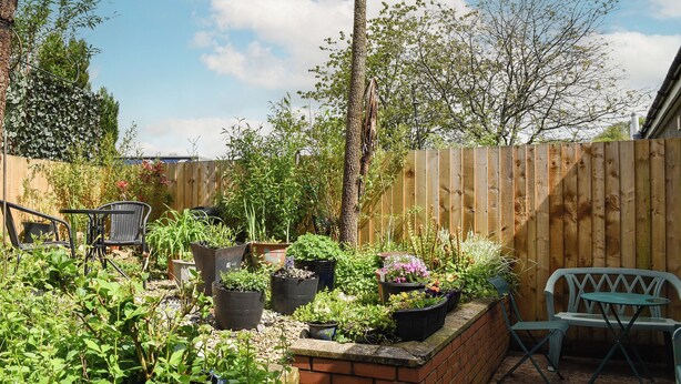 Ein Gartenbereich mit Topfpflanzen, einem Ziegelpflanzkübel und Gartenmöbeln.