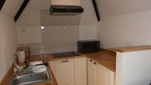 Una cocina compacta con pileta, microondas y placares blancos.