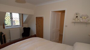 Un dormitorio con una cama grande, una silla, un radiador y una puerta que da a otra habitación.