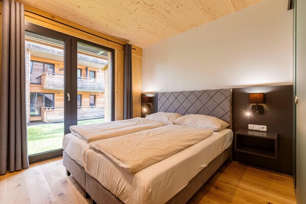 Une chambre avec deux lits, un plafond en bois, une grande fenêtre et une table de chevet avec une lampe.