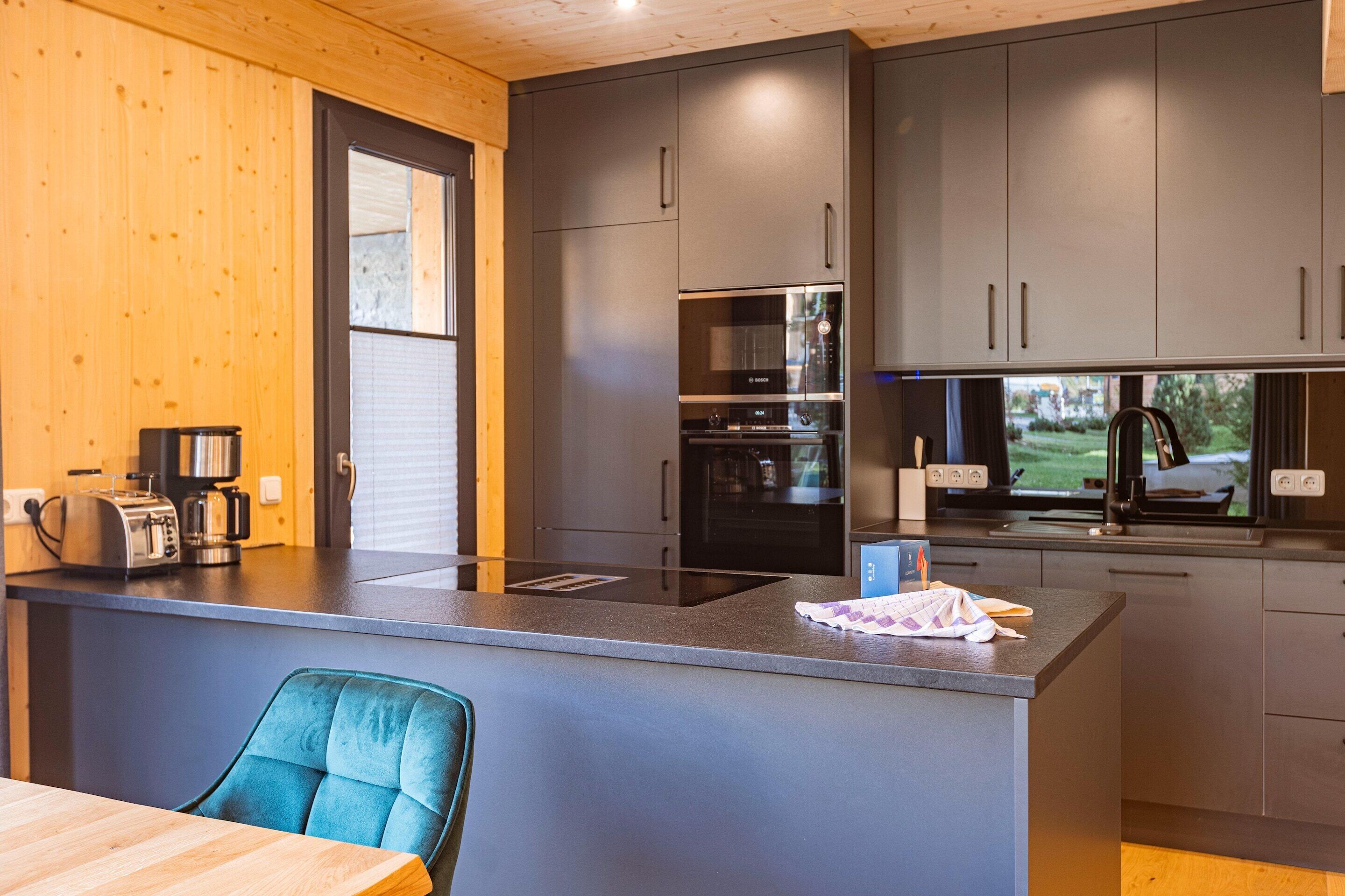 A modern kitchen with grey cabinets, a built-in oven, and a coffee maker.