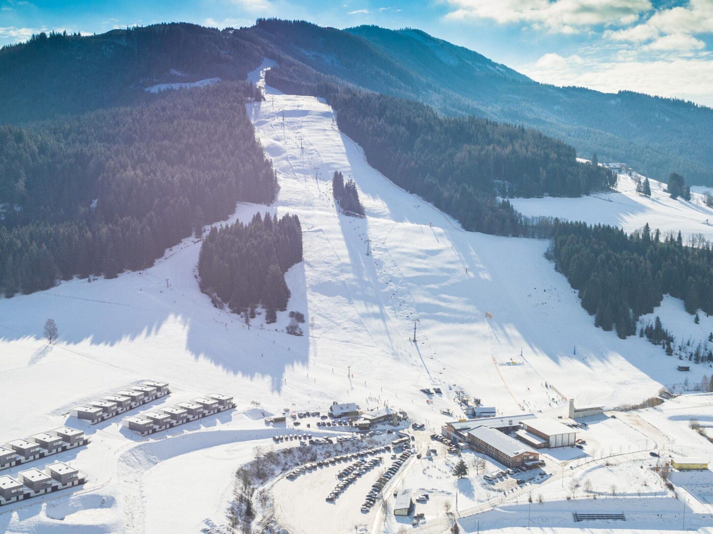 An aerial view of a ski resort with multiple buildings, parking areas, and a snow-covered landscape.