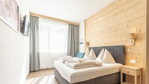 A modern hotel room with a large bed, wooden panel walls, a bedside table, and a window with curtains.