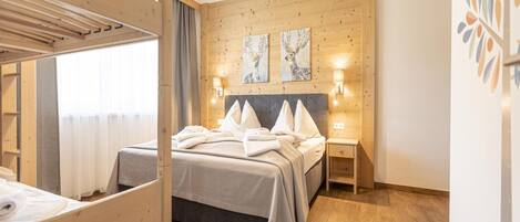 Habitación de hotel con una cama nido de madera, una cama individual y suelo de madera. Hay dos lámparas de pared y dos cuadros en la pared.