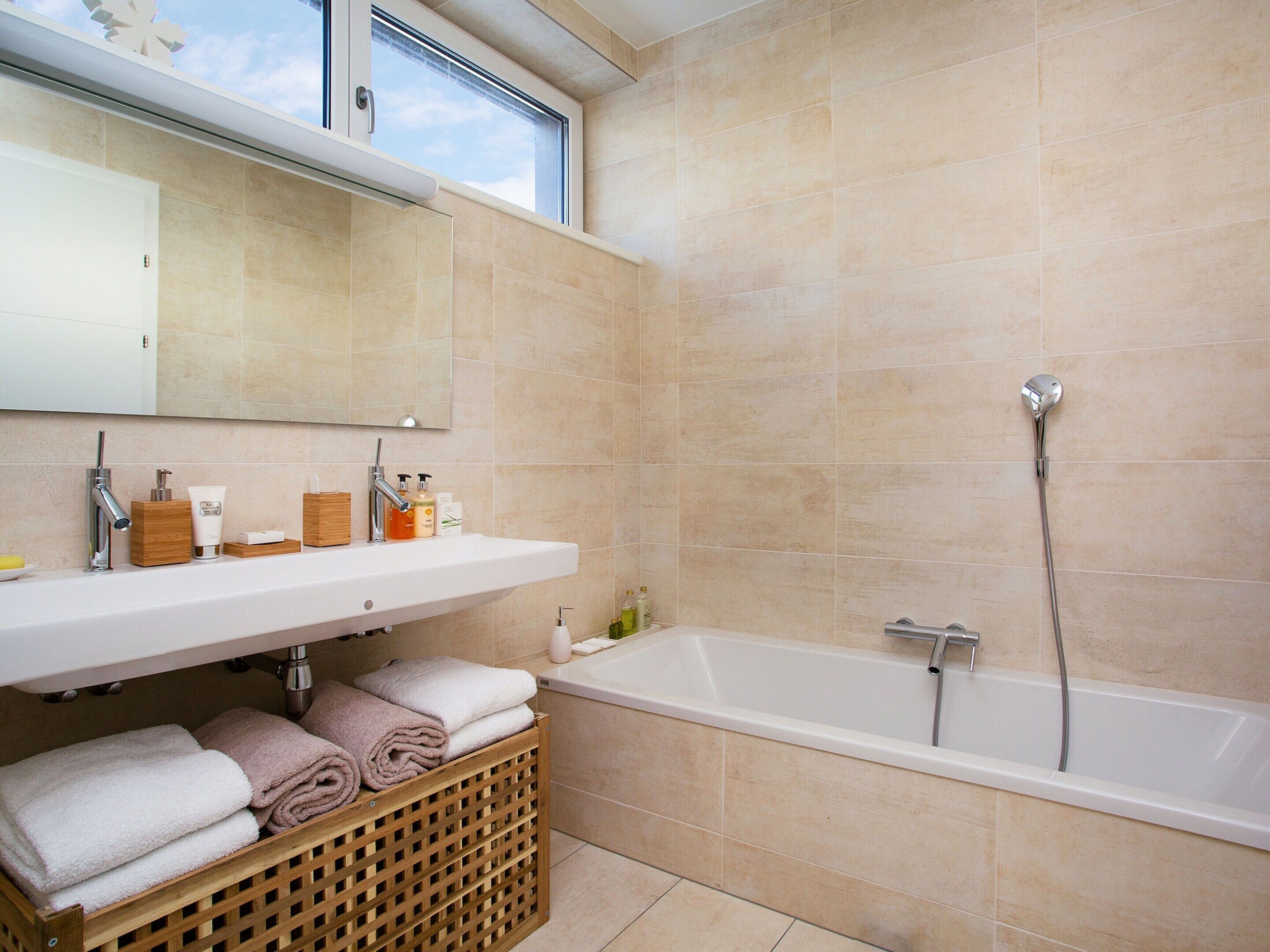 Une salle de bain moderne avec une grande baignoire, un lavabo avec un miroir au-dessus et une fenêtre située au-dessus du lavabo.