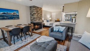 A modern living room with a fireplace, a dining area, a kitchen, and a bedroom. - Super Cozy Studio Near Slopes And Shuttle Bus WiFi (Snowshoe)