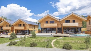 Een rij houten vakantiehuisjes met buitenmeubels en een zwembad.