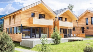 Een modern houten huis met balkon, grote ramen en een klein terras.