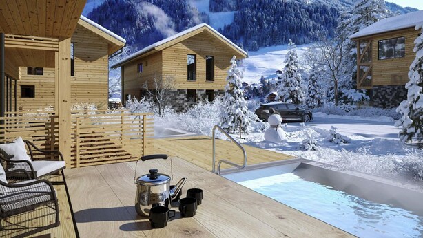 Een houten chalet met terras, een bubbelbad en uitzicht op besneeuwde bergen.