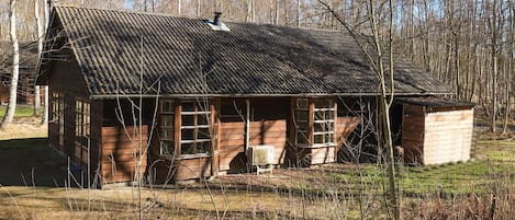 Een rustieke houten chalet met een schuin dak, grote ramen en een schoorsteen.