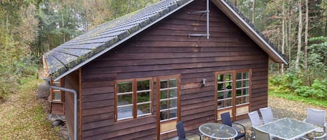 A rustic wooden cabin with a sloped roof, large windows, and a satellite dish.