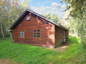 En stuga av trä med ett sadeltak, en veranda och ett litet fönster.