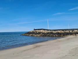 Uma paisagem costeira com um molhe rochoso e um céu azul límpido.