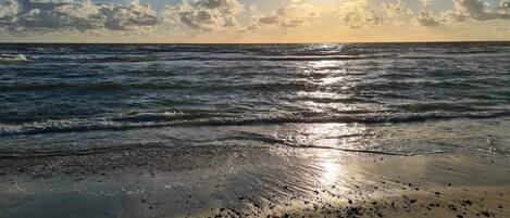 A beach with waves, pebbles, and a clear sky.