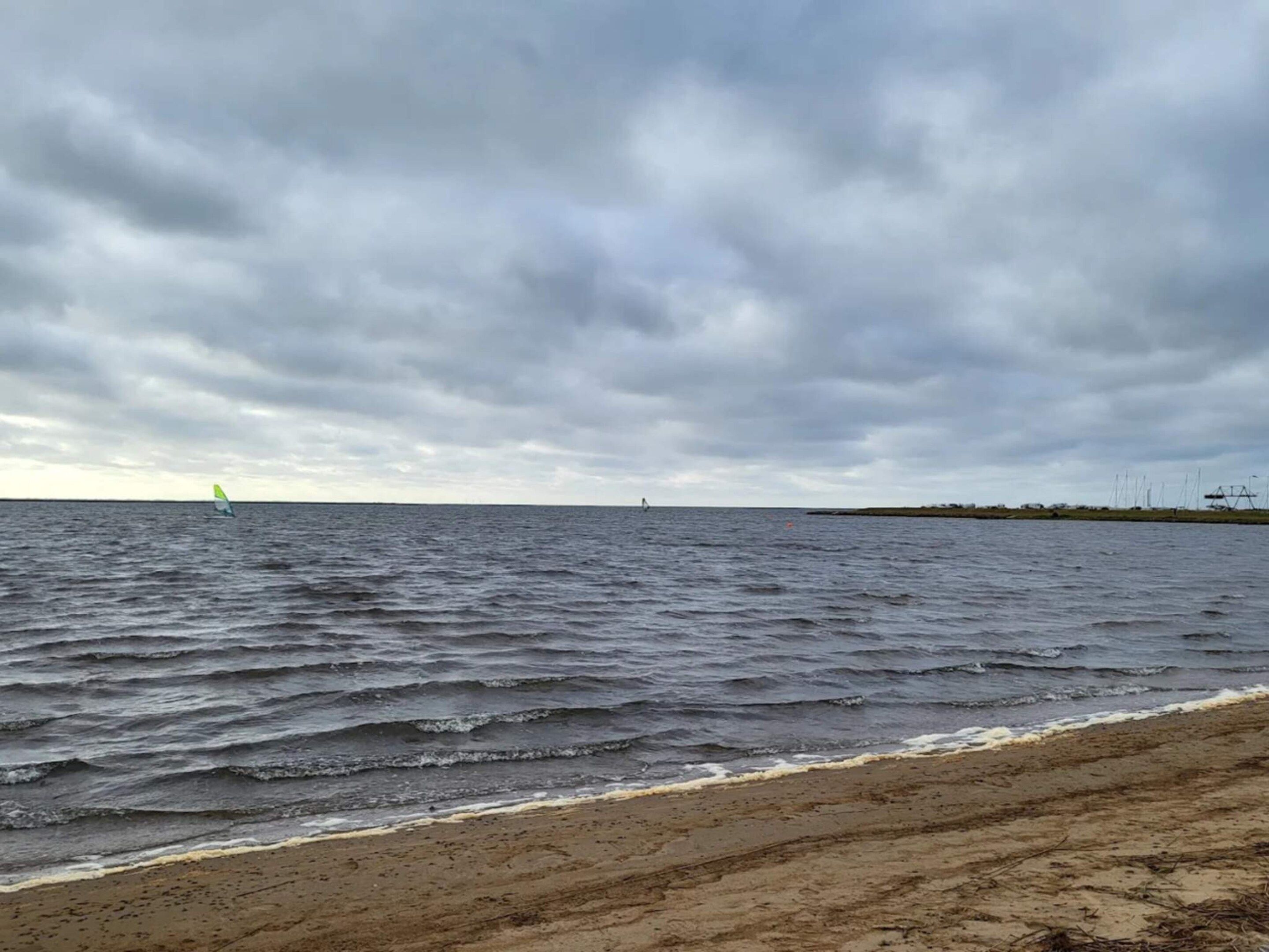A beach with waves, a distant sailboat, and a cloudy sky.