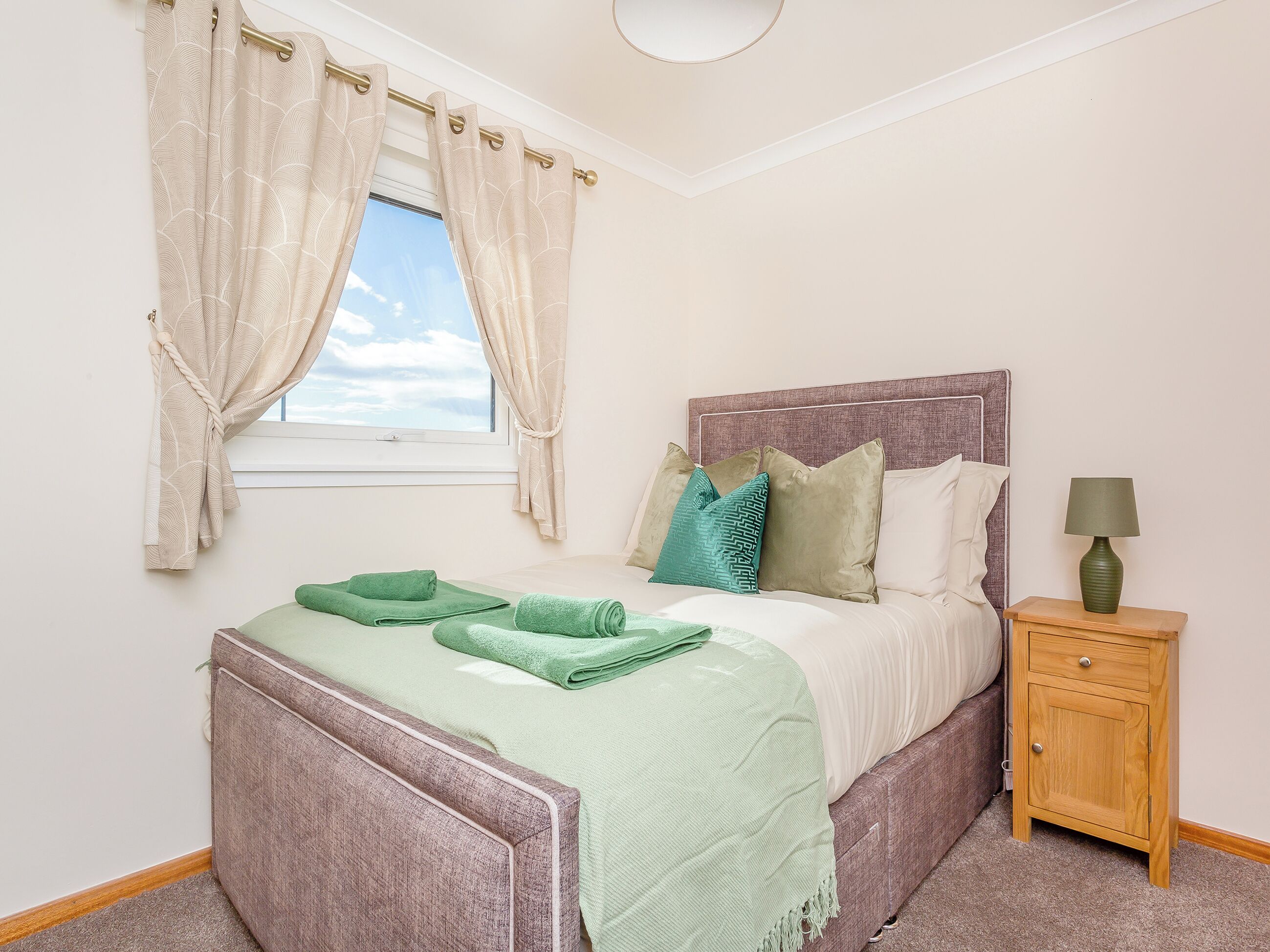 A bedroom with a bed, a nightstand, a lamp, and a window with curtains.