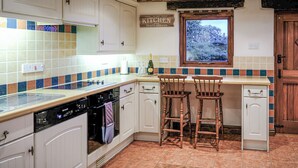 A kitchen with white cabinets, a tiled backsplash, wooden bar stools, and a window with a view of trees. - 1 bedroom accommodation in Combs, near Chapel-en-le-Frith (Combs, near Chapel-en-le-Frith)