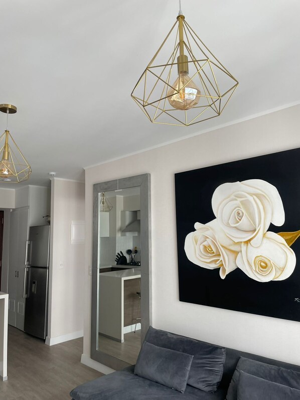 A modern living room with a grey sofa, a black and white rose painting, and a kitchen visible through an open door. - Stylish1BR with Private Balcony in Barranco (Lima)