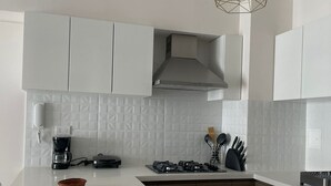 Uma cozinha moderna com armários brancos, fogão embutido, cafeteira e uma luminária pendente geométrica singular.