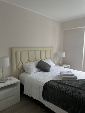 A neatly arranged bedroom with a tufted headboard, a white bedspread, a black throw blanket, and two bedside lamps. - Stylish1BR with Private Balcony in Barranco (Lima)