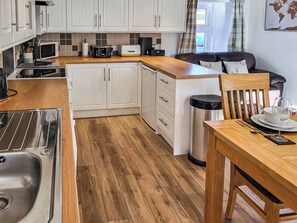 Une cuisine moderne avec des armoires blanches, un plan de travail en bois, un évier, une poubelle et un coin repas comprenant une table et des chaises.