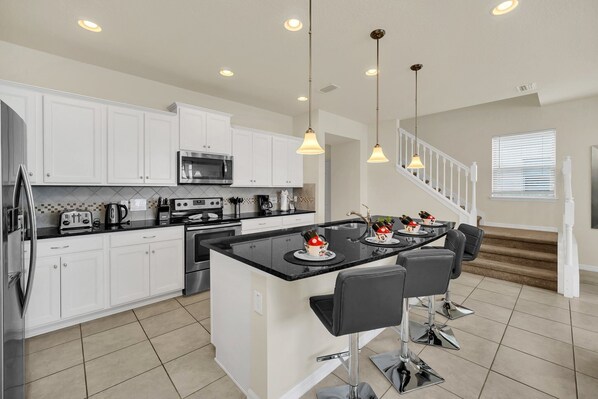 A modern kitchen with white cabinets, a central island, and a dining area with bar stools.