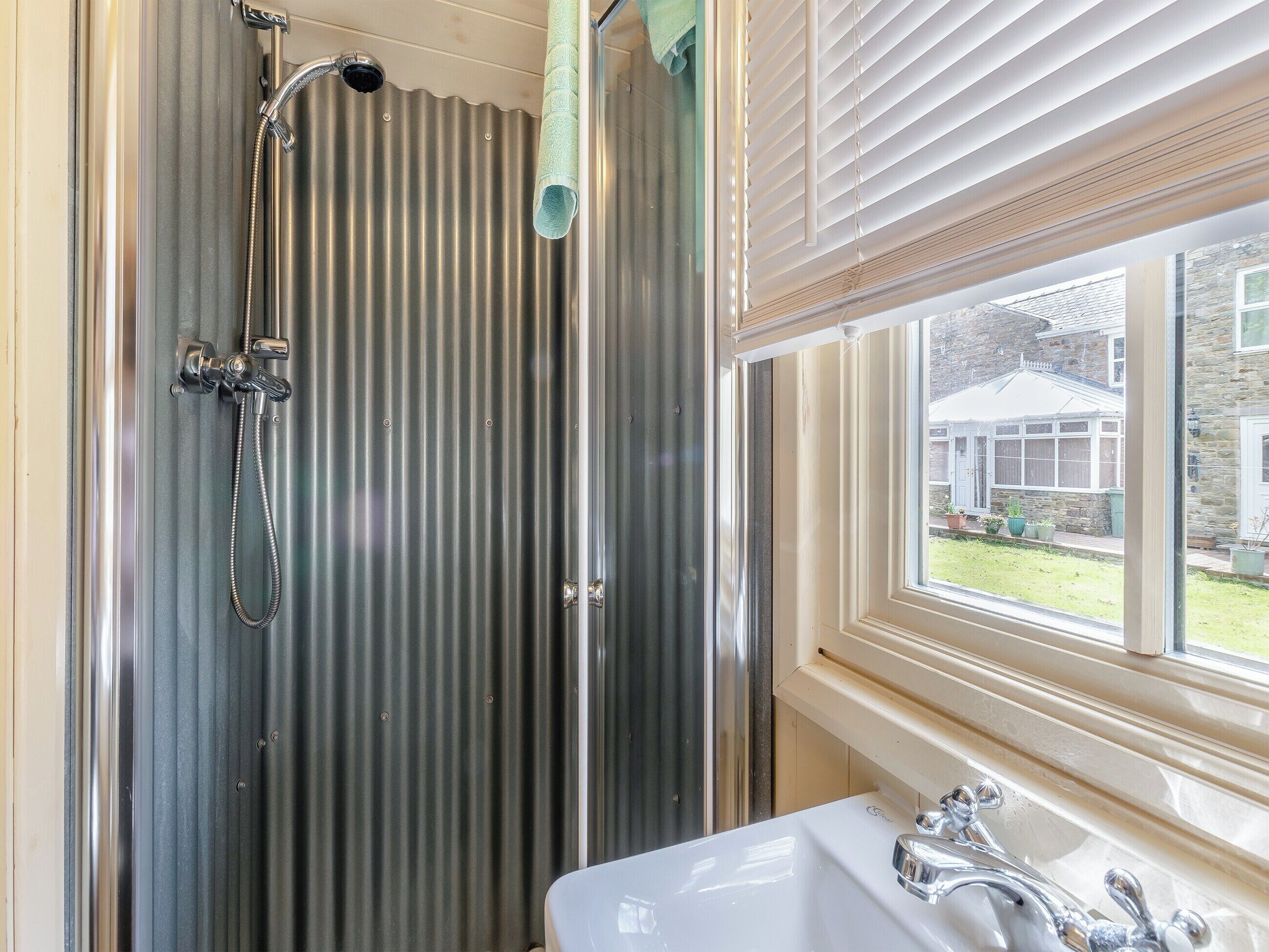 Une salle de bain avec une douche, un lavabo et une fenêtre donnant sur une maison.