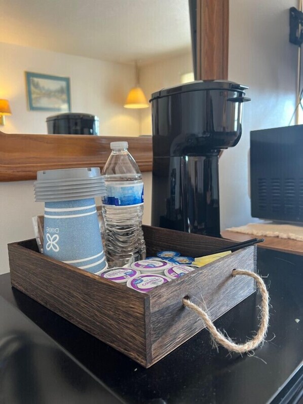 Una bandeja de madera con asa que contiene una toalla rayada, una botella de agua y una cafetera sobre una mesa.