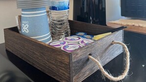 Un plateau en bois muni d’une anse, contenant une serviette à rayures, une bouteille d’eau et une cafetière, est posé sur une table.