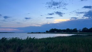 Un paysage côtier avec une étendue d’eau, des zones herbeuses et des arbres, le tout sous un ciel crépusculaire.