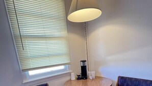 A small room with two wooden chairs, a round table, a floor lamp, and a window with blinds.
