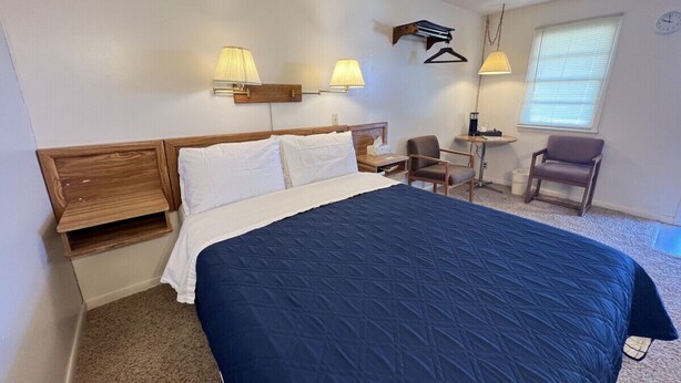 Una habitación de hotel con una cama grande, dos mesitas de noche, una silla, una pequeña mesa y una lámpara.