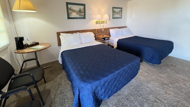A hotel room with two beds, a small table with a lamp, a chair, and a picture on the wall. - Room 114 - Double Full - Sleeps 4 - West Lake Grandvue Inn (Downs)