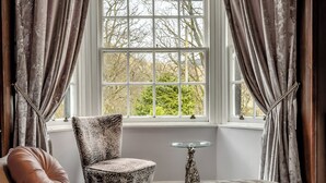 Ein Schlafzimmer mit einem Bett, einem Sessel, einem kleinen Tisch und einem Fenster mit Vorhängen.