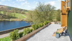 A building with a wooden deck overlooking a body of water and a green field. - Keepers Hide - UK43676 (Oldfield, near Keighley)