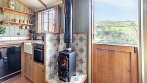 A kitchen with a wood-burning stove, wooden cabinets, and a view of the countryside. - Keepers Hide - UK43676 (Oldfield, near Keighley)