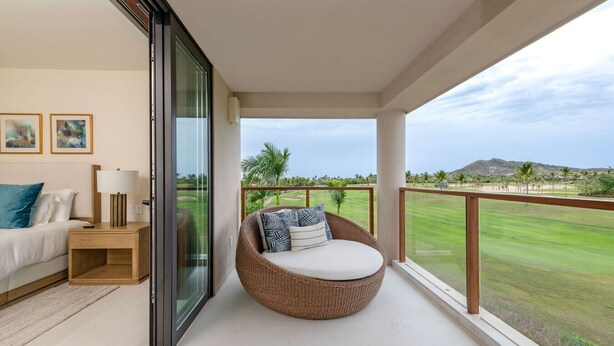 Un balcón con una silla de mimbre, una cama con una mesita de noche y vista a un campo de golf.
