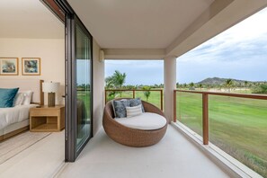 Un balcón con una silla de mimbre, una cama con una mesita de noche y vista a un campo de golf.