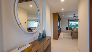 Un pasillo moderno con una consola de madera, un espejo grande y vistas a una sala de estar con sofá y televisión.